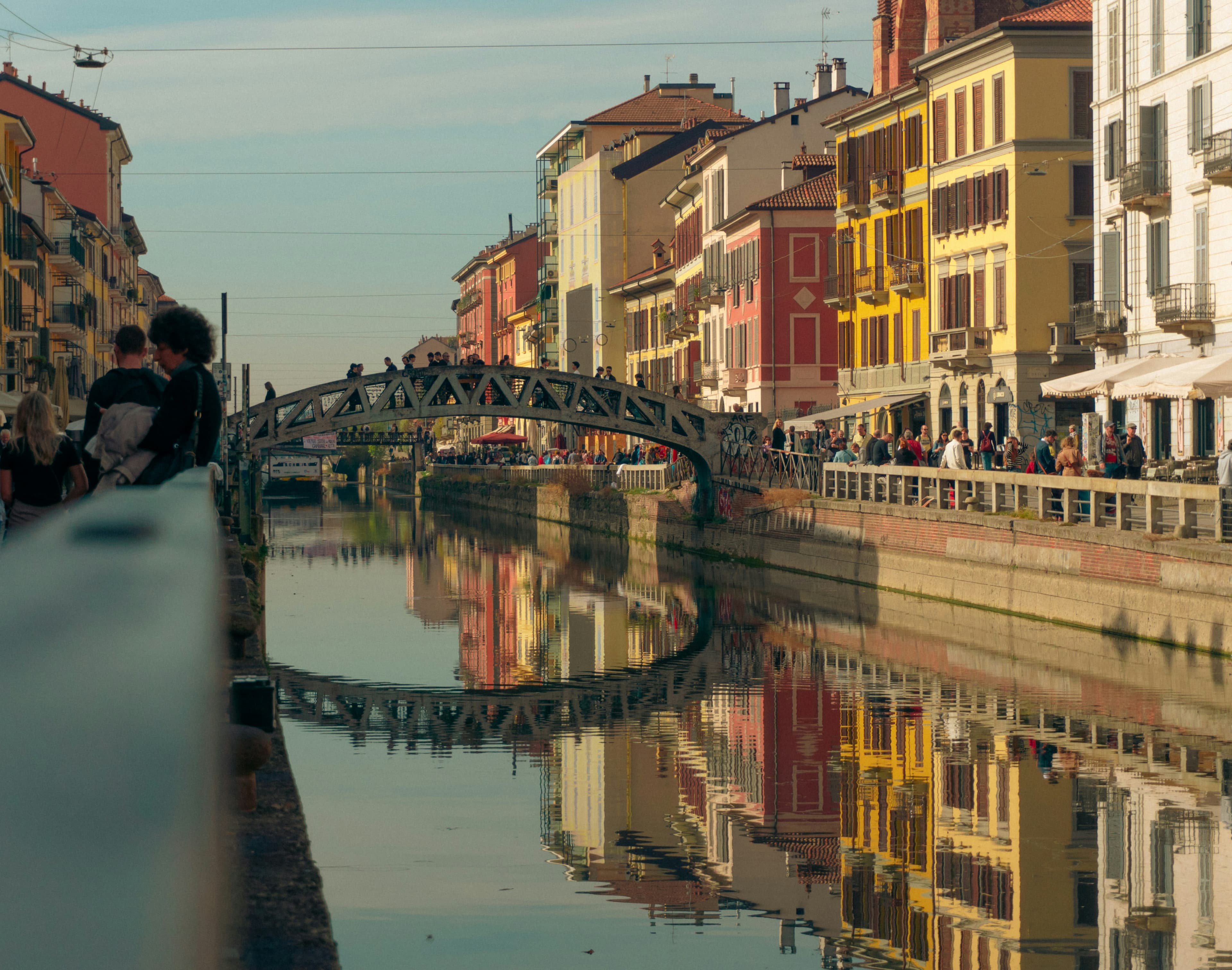 An iron footbridge over a canal in Milan, the houses reflected in the water