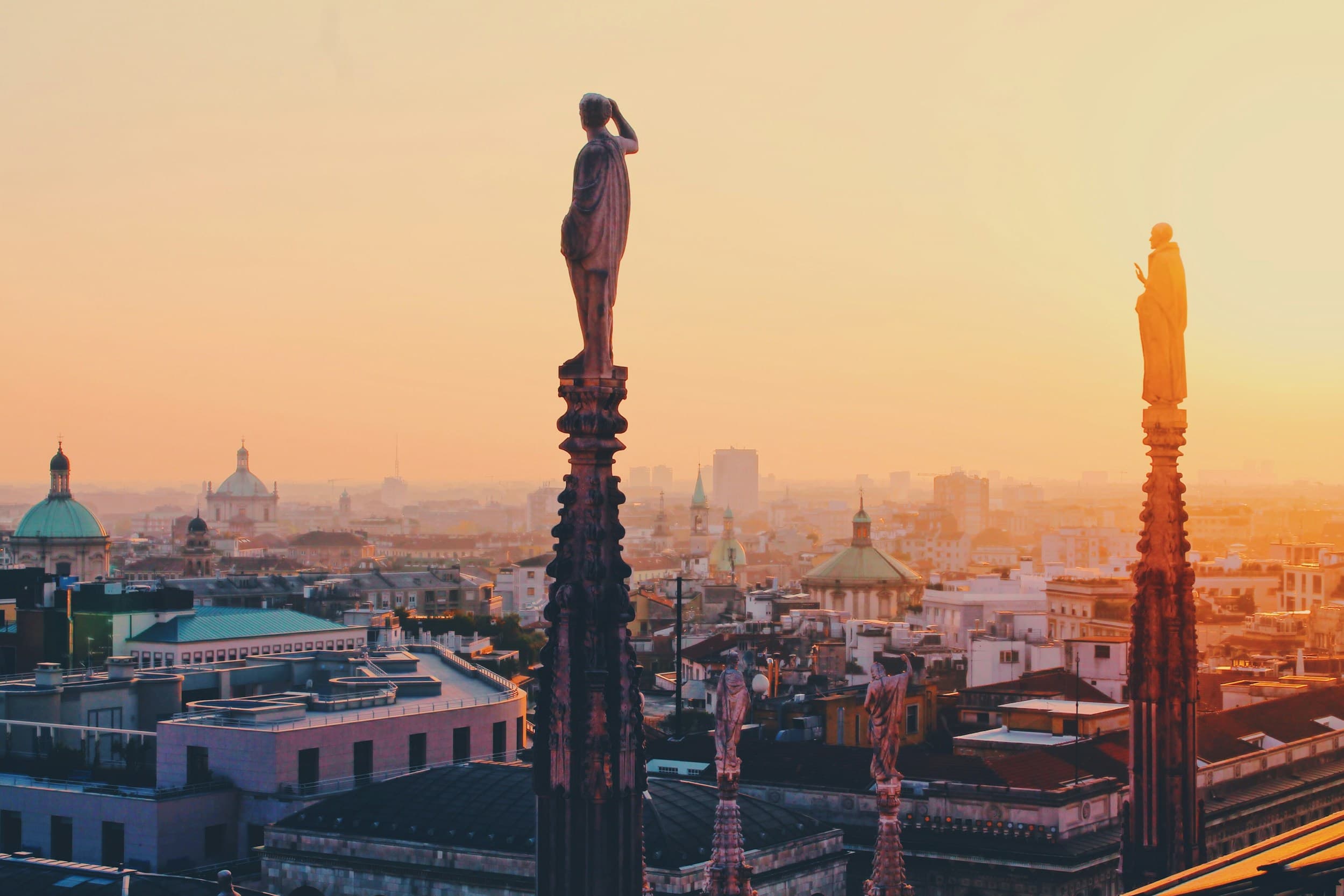 Statues on the spires of Milan Cathedral above the city at sunset