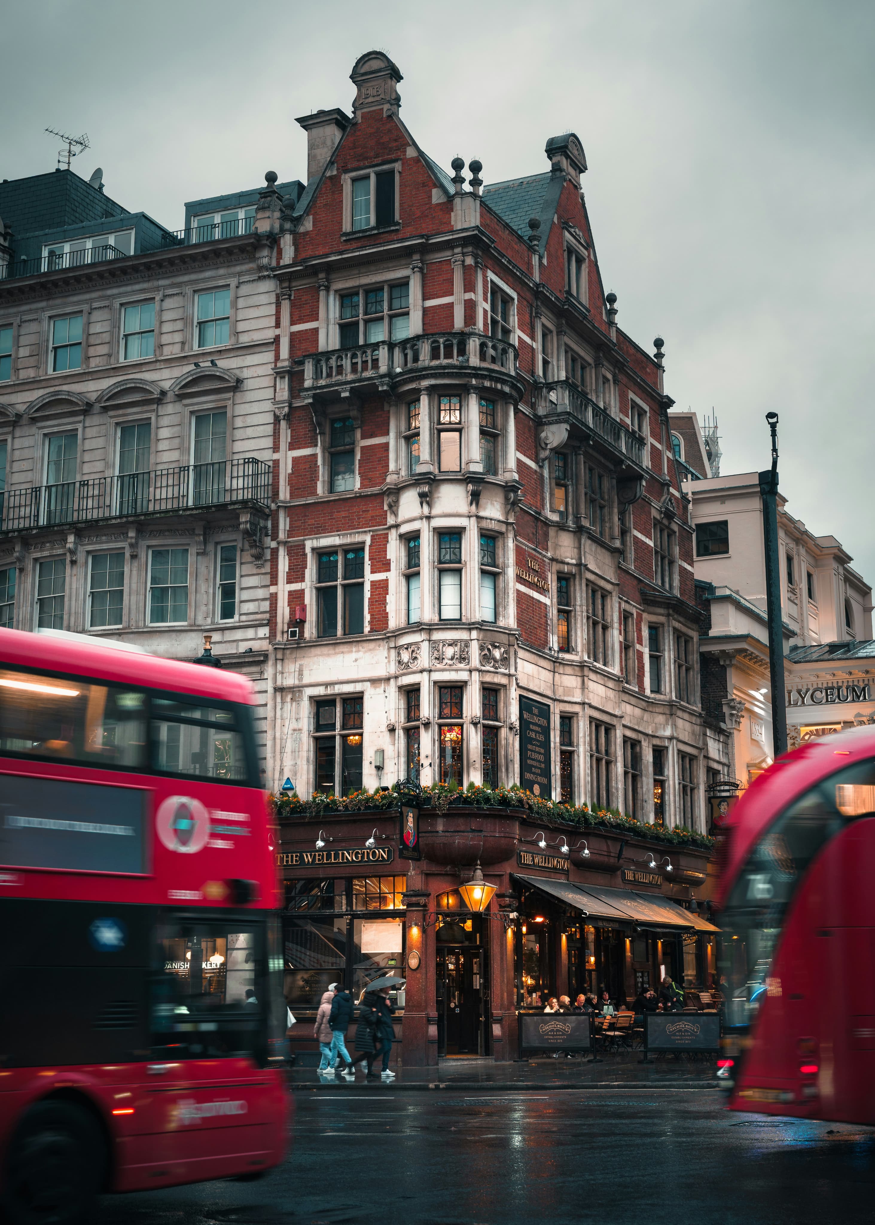 Red buses passing a Victorian pub on a London corner in the rain