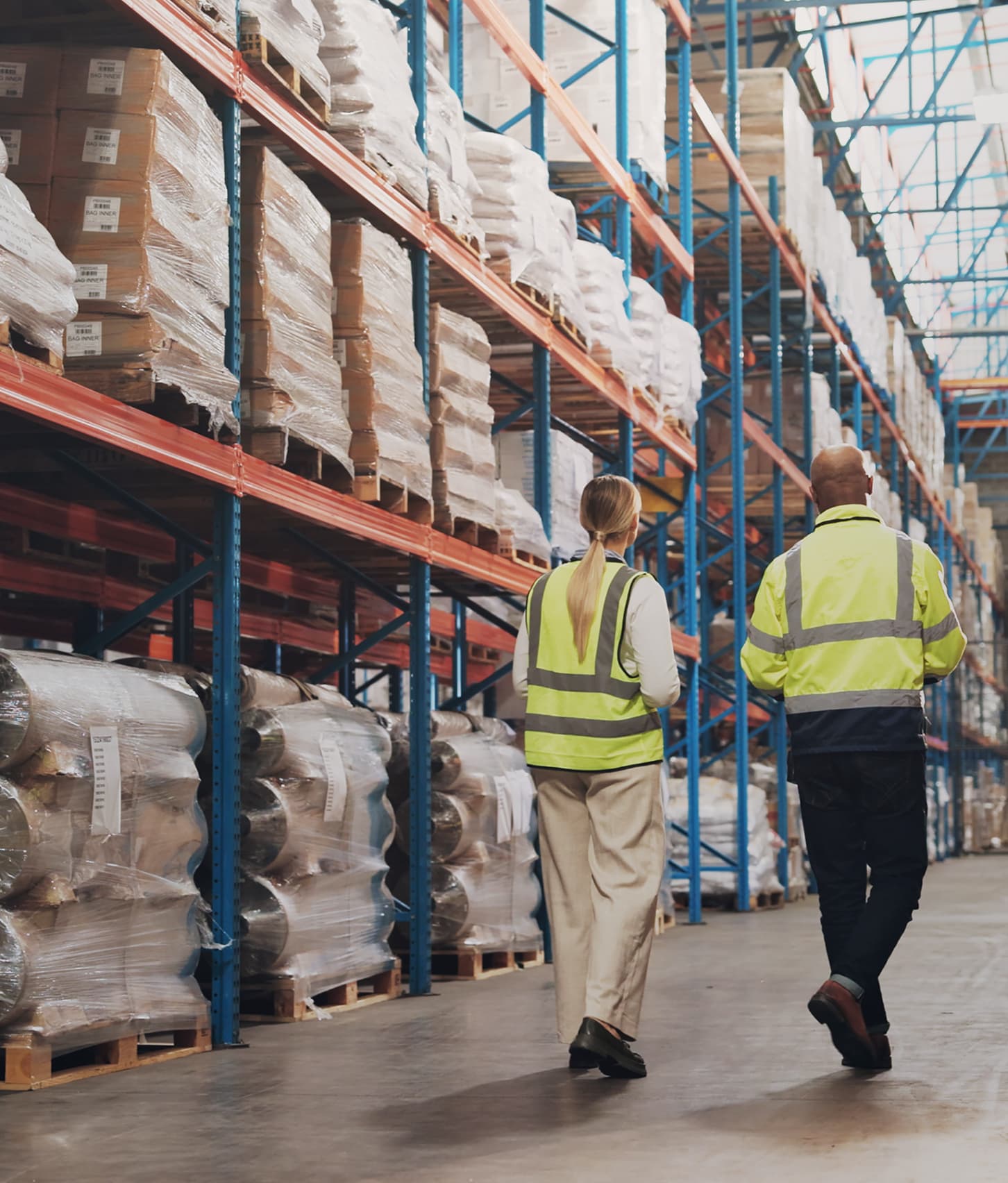 Two workers in hi-vis jackets walking down a warehouse aisle