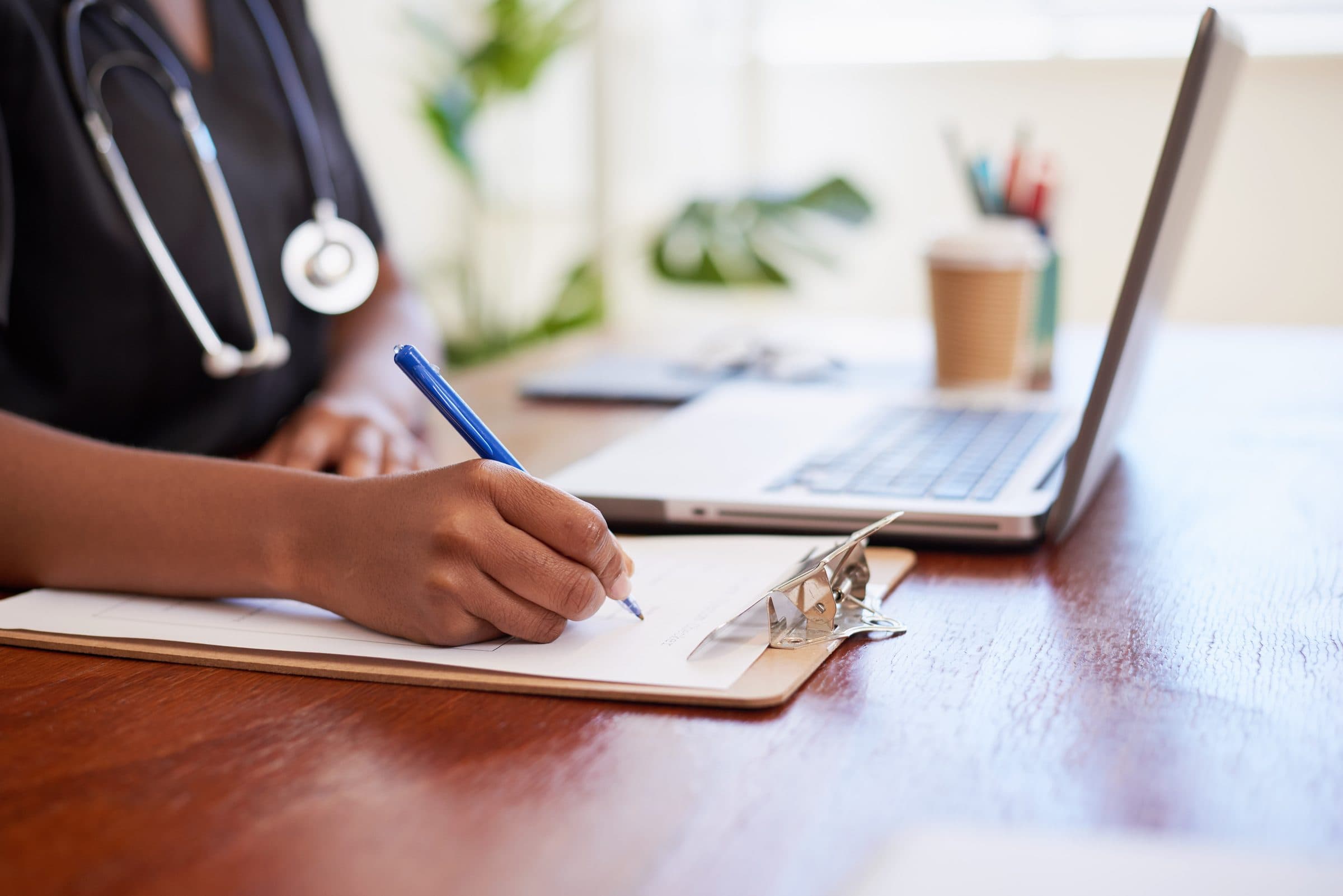 A doctor writing notes beside a laptop